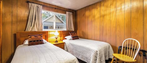Een kamer met twee bedden, een nachtkastje met lamp, een stoel en houten wanden.
