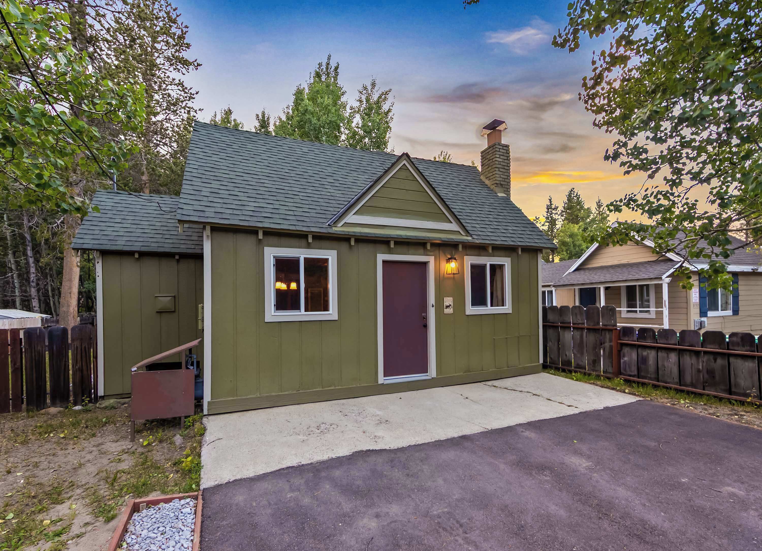 A small, single-story house with a green exterior, a dark red door, and a small porch area.