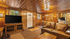 A cozy living room with a television, leather sofa, wooden coffee table, and a chandelier. - Paradise Bungalow - Cozy Cabin Escape (South Lake Tahoe)