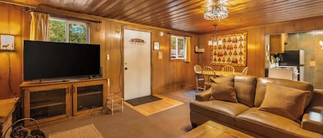A cozy living room with a television, leather sofa, wooden coffee table, and a chandelier.