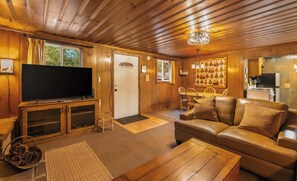 A cozy living room with a television, leather sofa, wooden coffee table, and a chandelier. - Paradise Bungalow - Cozy Cabin Escape (South Lake Tahoe)