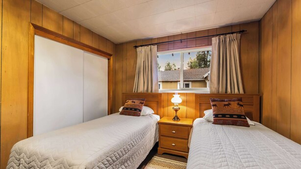 A room with two beds, wooden walls, a window with curtains, and a bedside lamp. - Paradise Bungalow - Cozy Cabin Escape (South Lake Tahoe)