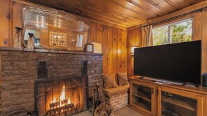 A cozy living room with a fireplace, a television, and wooden paneling. - Paradise Bungalow - Cozy Cabin Escape (South Lake Tahoe)