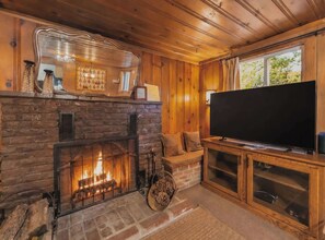 A cozy living room with a fireplace, a television, and wooden paneling. - Paradise Bungalow - Cozy Cabin Escape (South Lake Tahoe)