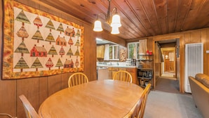 A wooden interior with a dining table, chairs, a kitchen area, and a large quilt on the wall. - Paradise Bungalow - Cozy Cabin Escape (South Lake Tahoe)