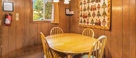 Habitación con paneles de madera, una mesa redonda y sillas, un extintor, una ventana con cortinas y un tapiz acolchado en la pared.
