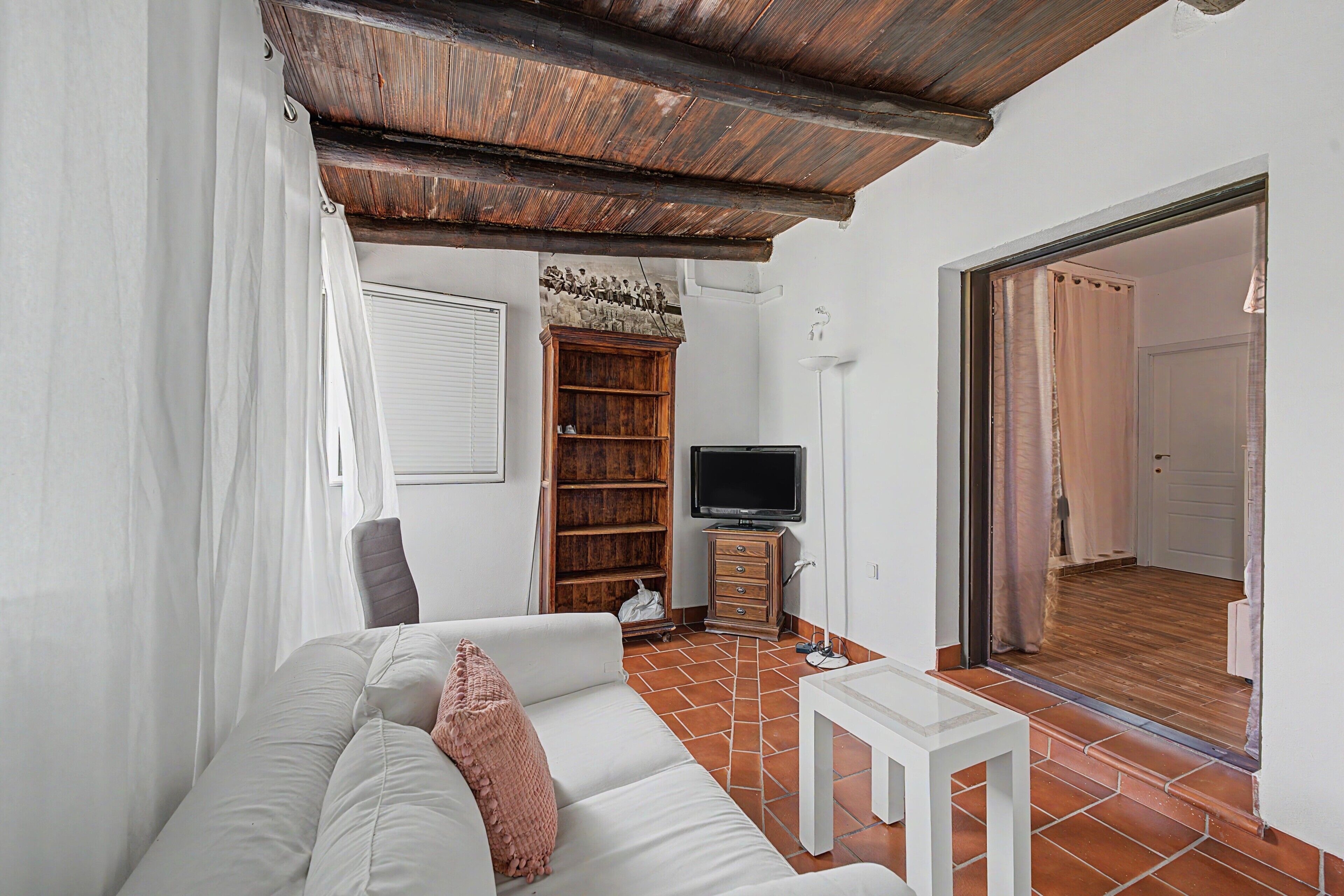 A living room with a white sofa, a television on a wooden stand, and a bookshelf.