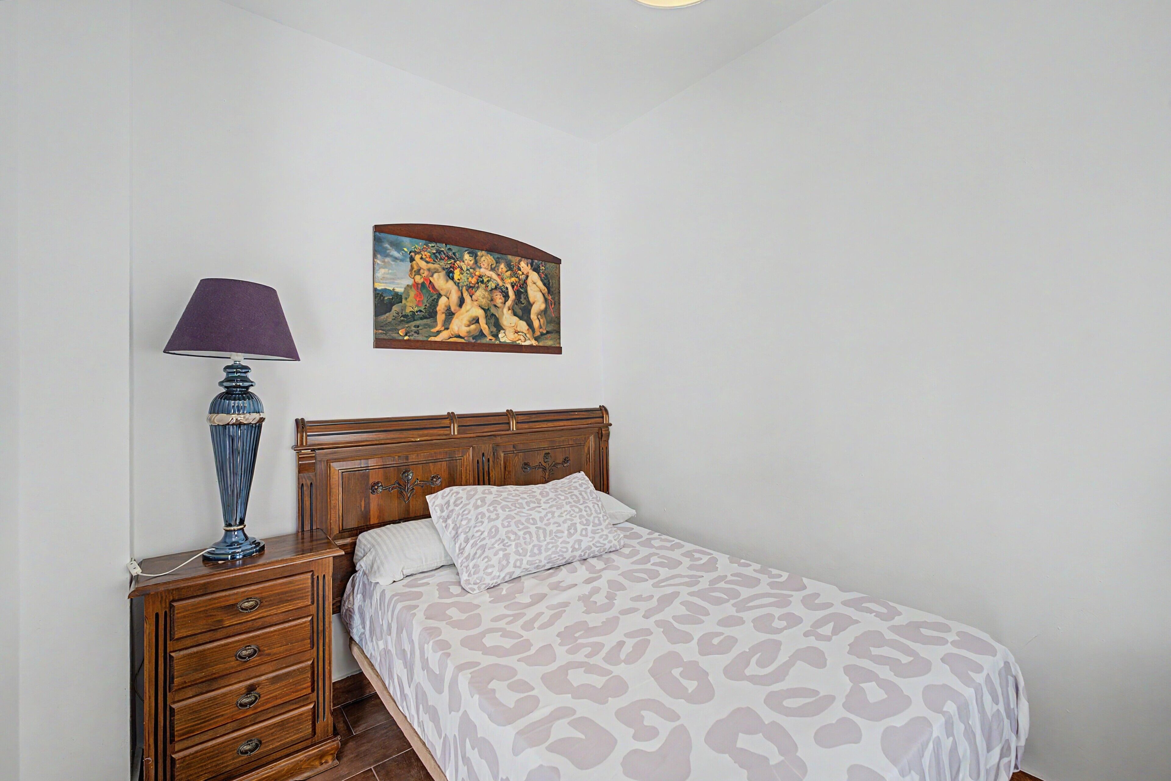 Un dormitorio con cama de madera, una mesita de noche, una lámpara y un cuadro en la pared.