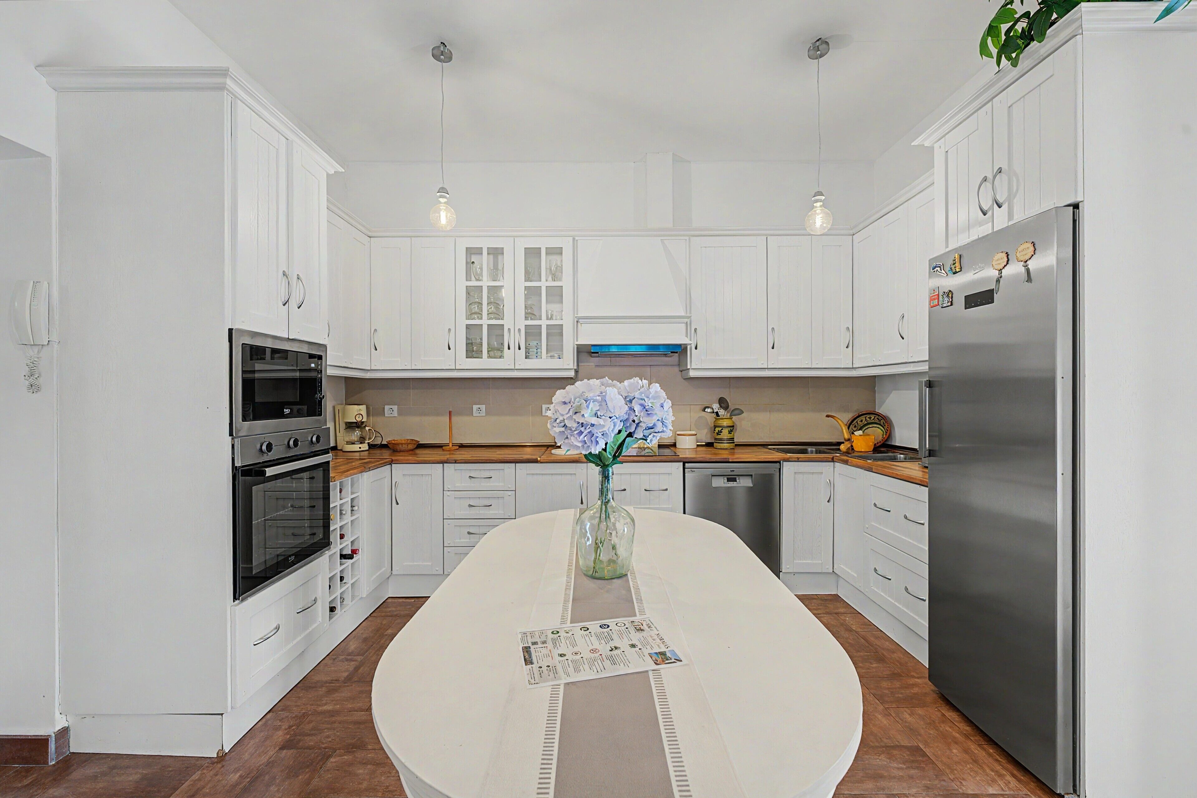 A modern kitchen with white cabinetry, stainless steel appliances, and a central island with a vase of flowers.