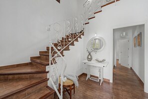 A staircase with a white metal railing, a wooden floor, a white console table with a mirror, and a door leading to another room.