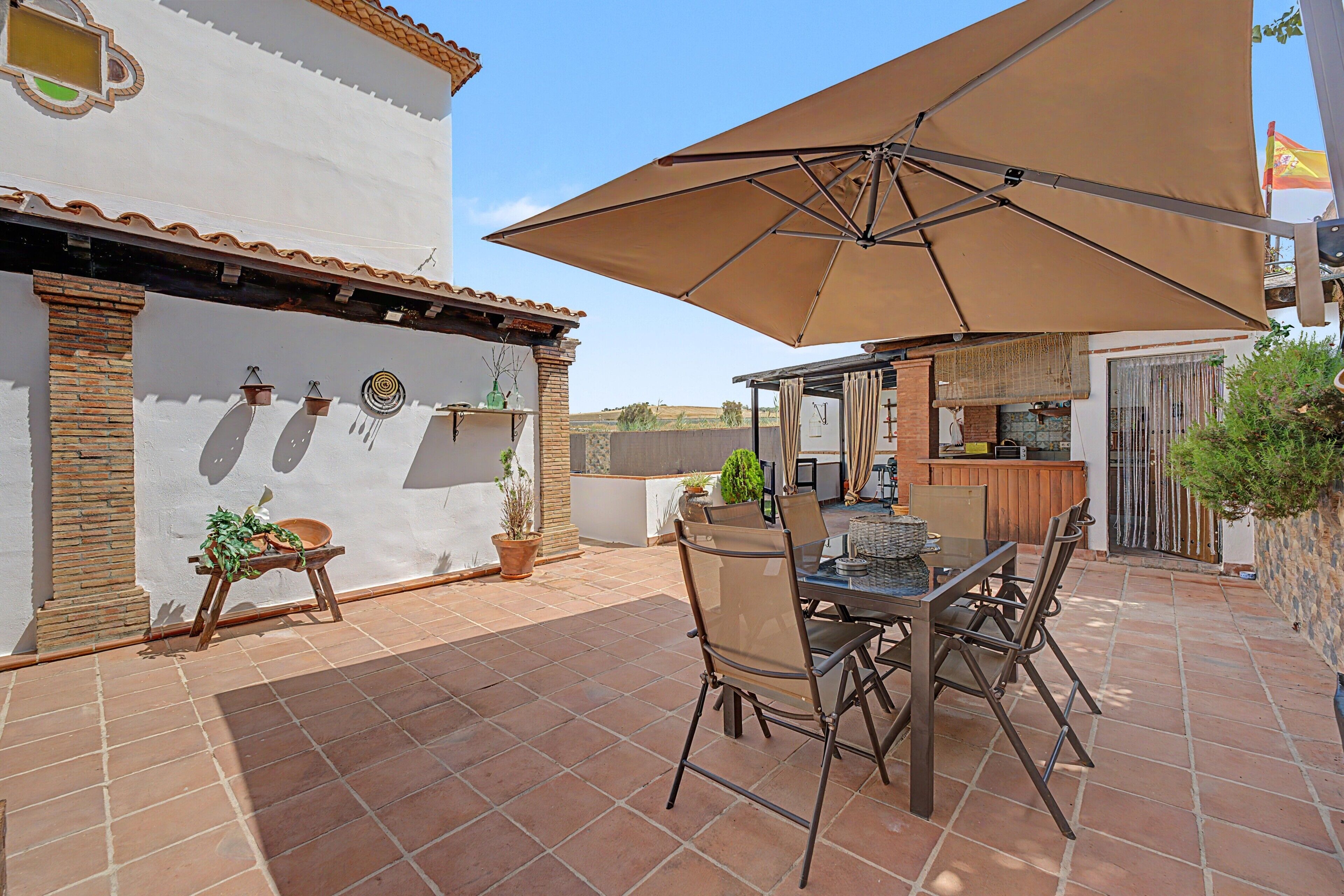 Un patio al aire libre con una mesa, sillas, un paraguas grande y un muro de ladrillo con detalles decorativos.