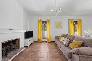 A living room with a fireplace, a sofa, a television, and yellow curtains.