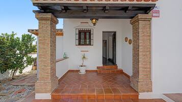 A building entrance with a tiled patio, a potted plant, and a window with bars.