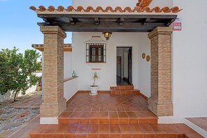A building entrance with a tiled patio, a potted plant, and a window with bars.