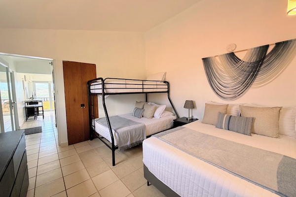 Spacious bedroom with queen bed, bunk beds, and tall ceilings. A/C and full attached bathroom
