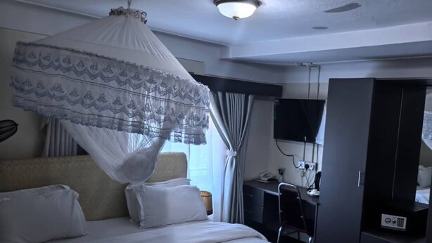 A hotel room with a bed, a desk, a wardrobe, and a television. - KAA HIGHWAY HOTEL (Mukono)