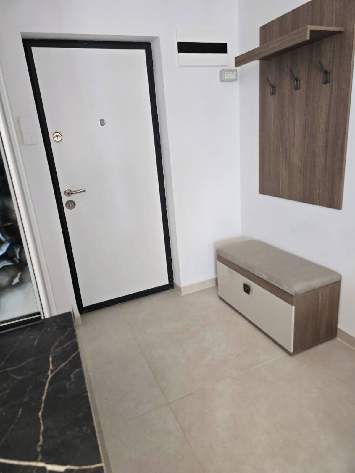 A room with a white door, a bench, a wall-mounted shelf with hooks, and a tiled floor.