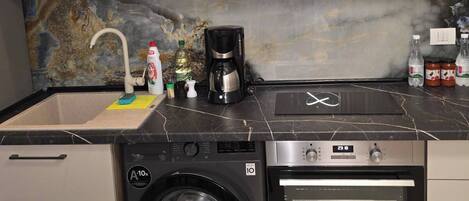 A compact kitchen with a washing machine, a coffee maker, and a microwave.