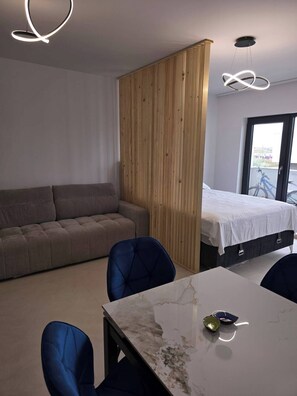 A modern room with a sofa, a bed, a dining table, and a wooden partition.