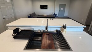 Una cocina moderna con una isla grande, horno empotrado y comedor con televisor de pantalla plana.