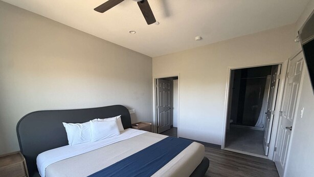 Un dormitorio con cama, mesita de noche, ventilador de techo y puerta corrediza que da a un baño.