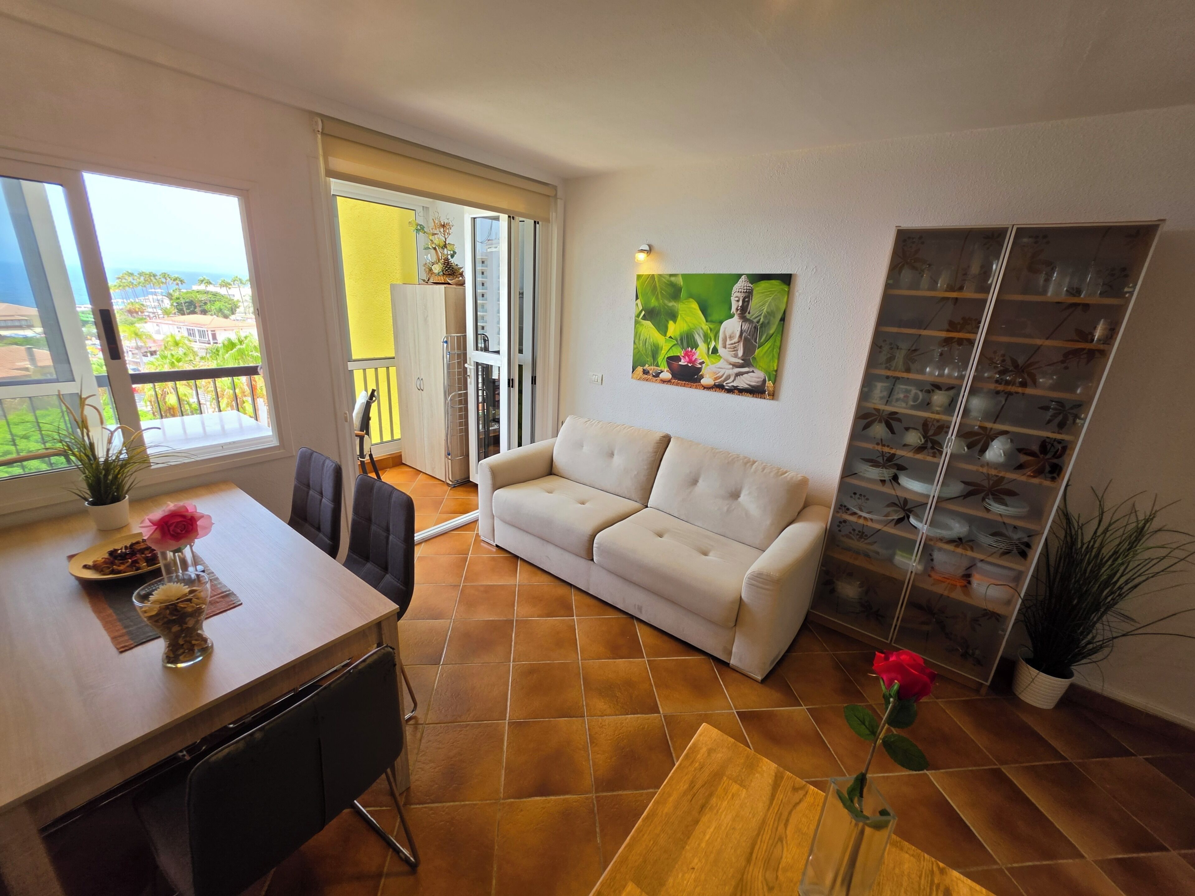 Ein Wohnzimmer mit Sofa, einem Esstisch mit Stühlen, einer Küchenzeile und einem Balkon mit Blick.