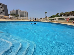 Ein Schwimmbecken mit klarem, blauem Wasser, umgeben von Liegestühlen und Sonnenschirmen.