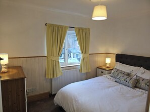A bedroom with a bed, bedside lamps, a window with curtains, a radiator, and a wooden nightstand. - Twisted Chimney View (Alford)