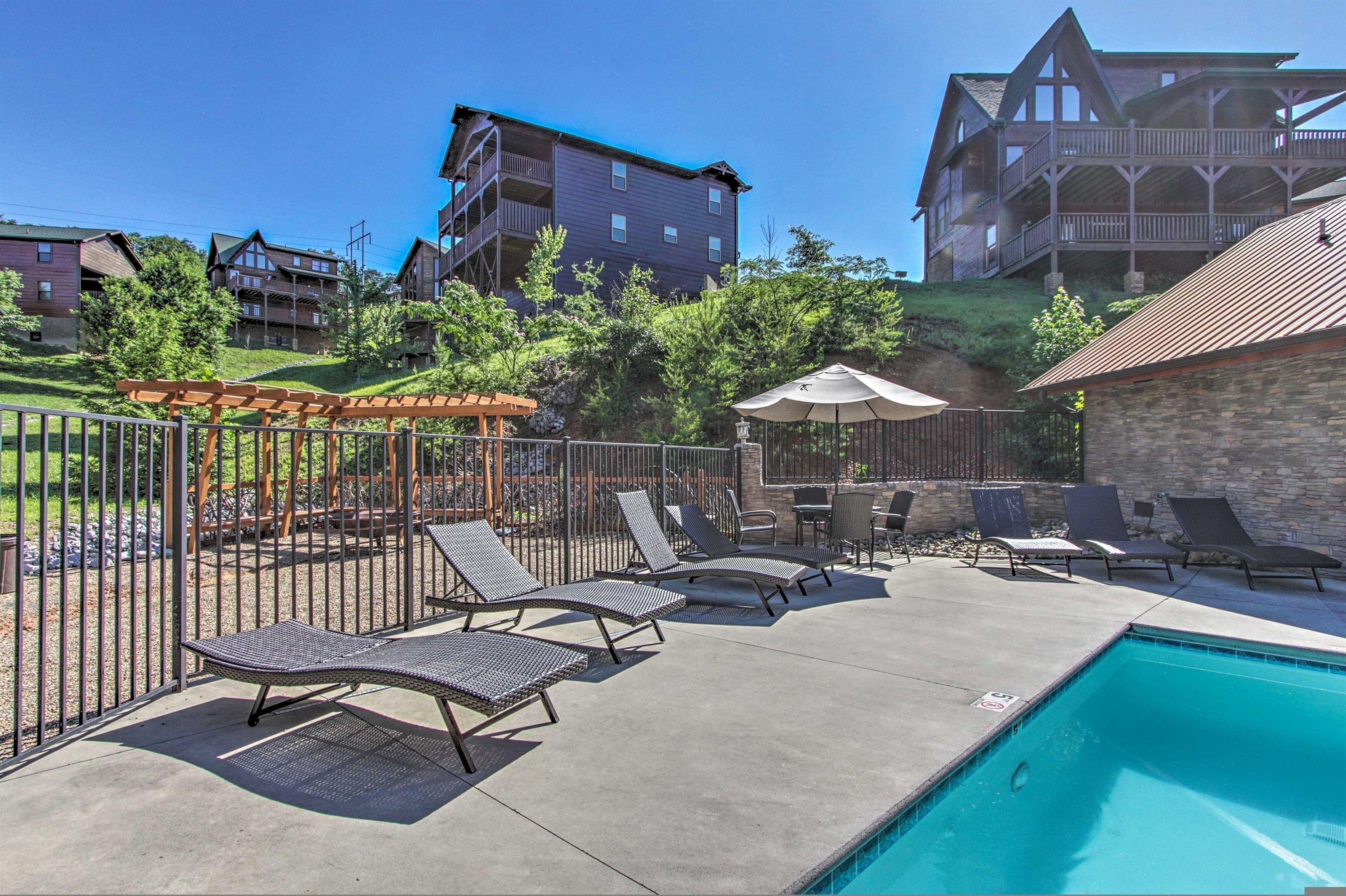 A poolside area with lounge chairs, a pergola, and a view of surrounding buildings.