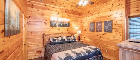 A wooden cabin bedroom with a bed, a ceiling fan, and wall-mounted artwork.
