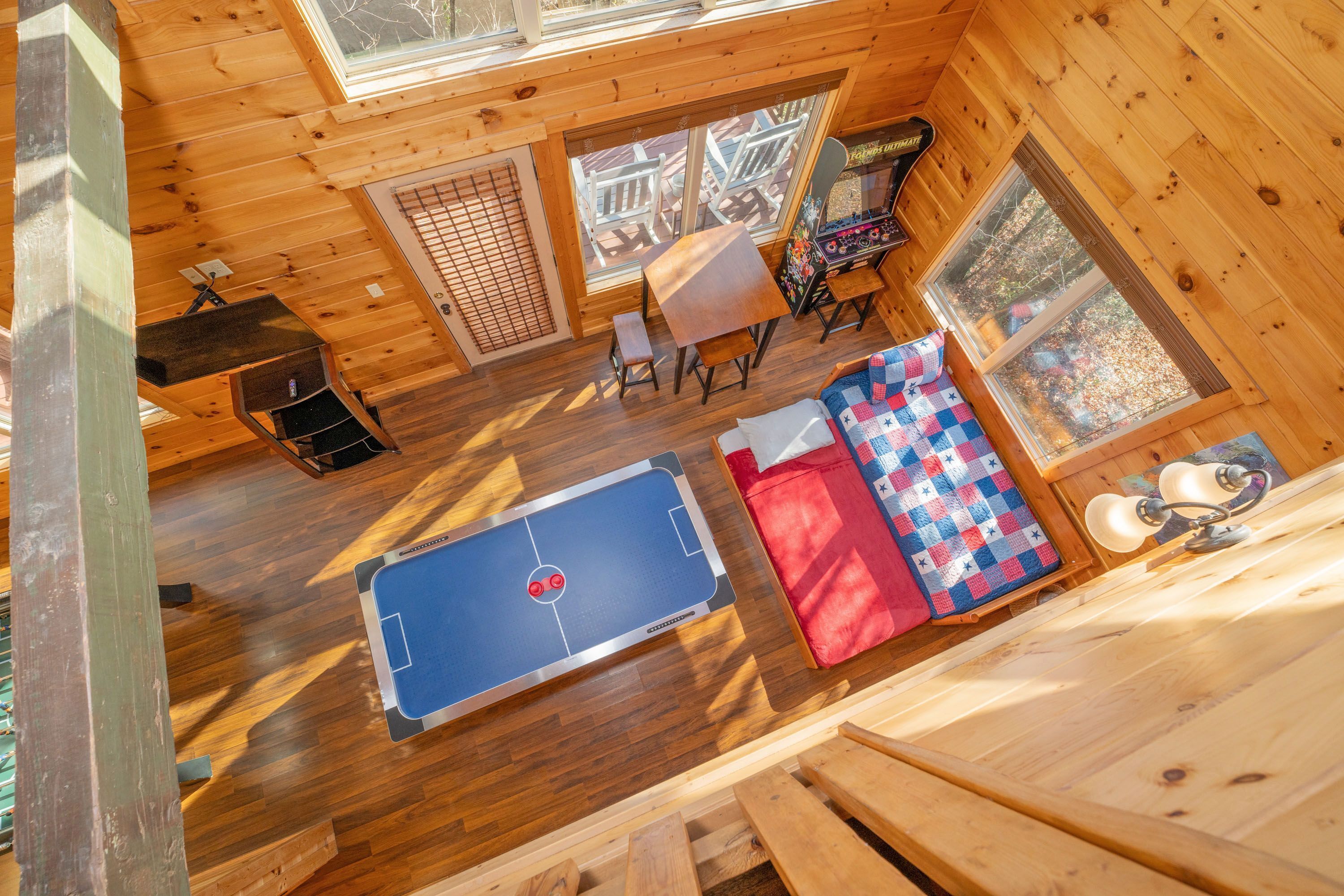 A wooden cabin interior with a ping pong table, a bench, a table with a game, and a window with a view.