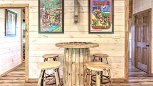 A wooden interior with a round table and stools, framed posters of 'Congo Bongo' and 'Mario Bros.' on the wall. - All Decked Out in Pigeon Forge (Pigeon Forge)