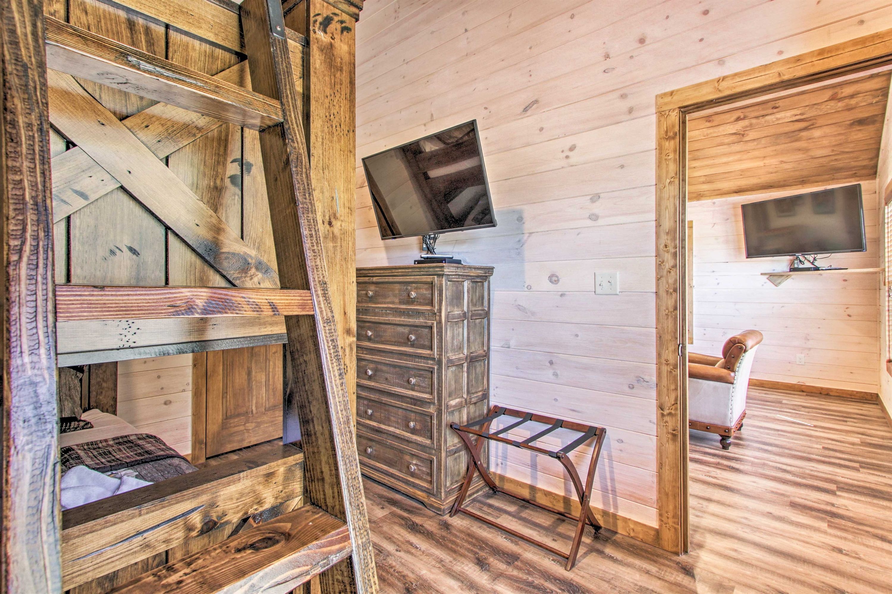 A rustic wooden room with a loft bed, a dresser, and two wall-mounted televisions.