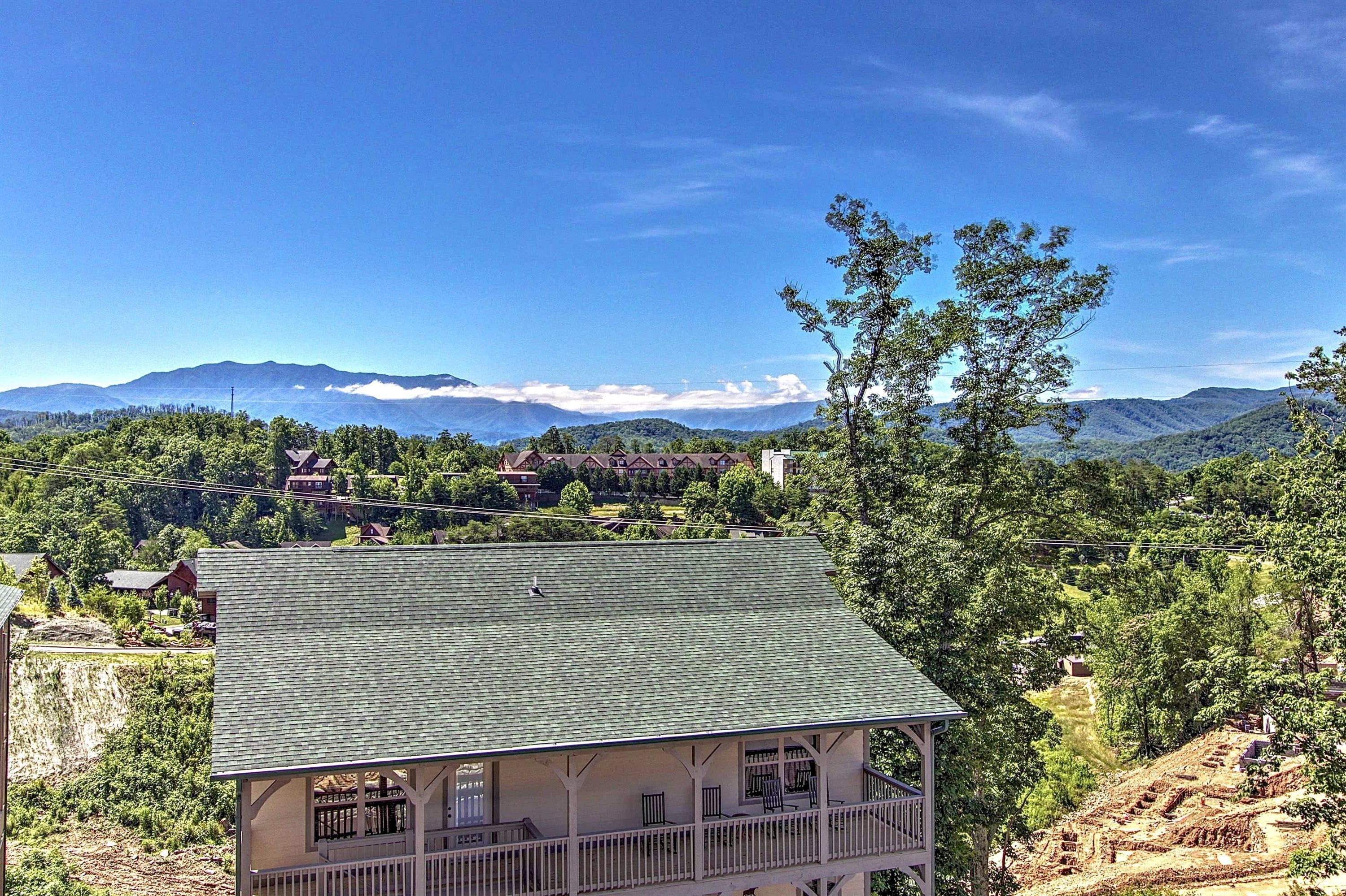 A two-story house with a green roof, a balcony, and a view of a mountainous landscape.