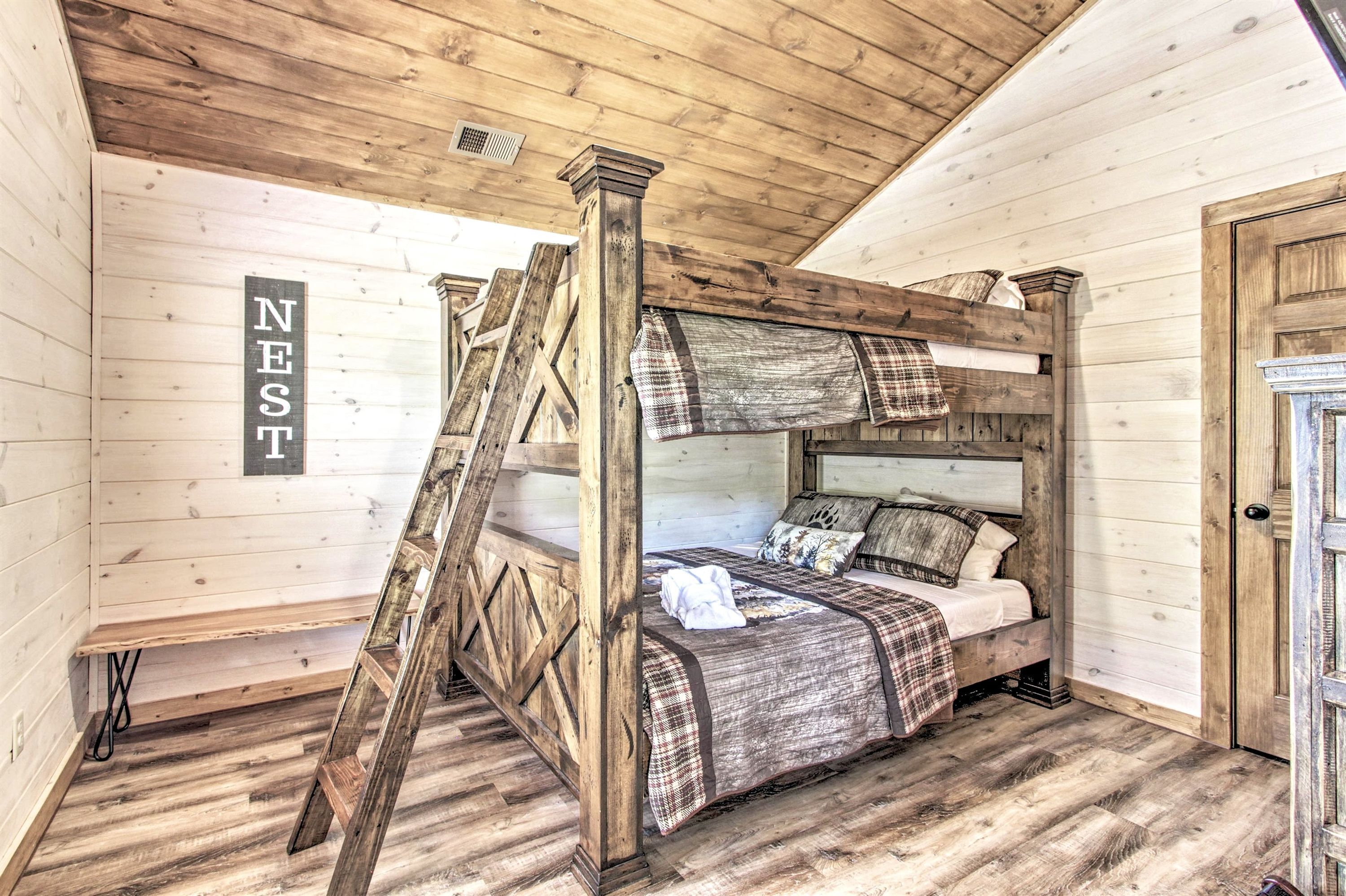 Una habitación rústica de madera con una cama estilo loft, una escalera y un letrero que dice 'NEST'.