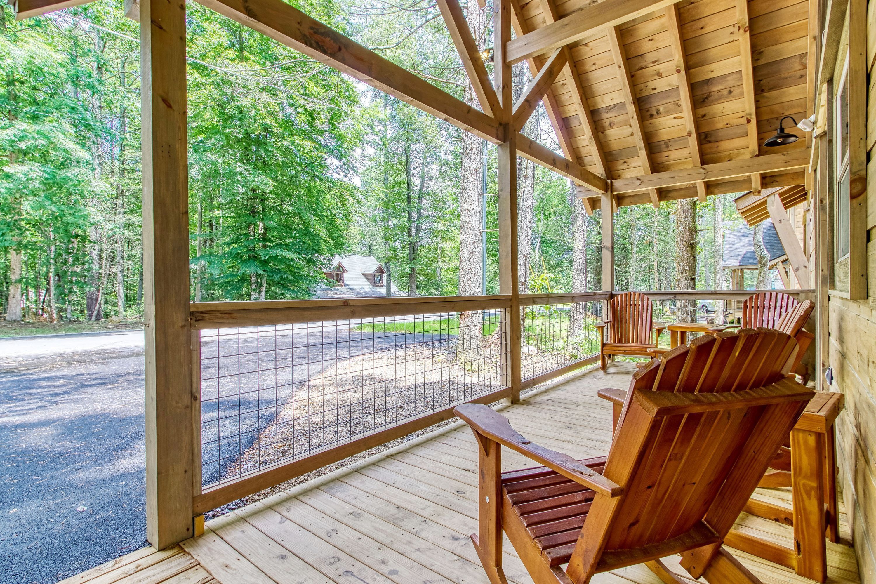 Een houten terras met Adirondack stoelen, een overdekt gedeelte met uitzicht op een bebost gebied.
