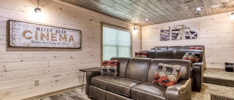 A cozy cinema-themed room with a leather sofa, wooden walls, and a sign reading 'WATER BEAR CINEMA.'