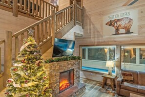 Interior de madera con chimenea, un árbol de Navidad, una escalera y decoración de pared con temática de osos.