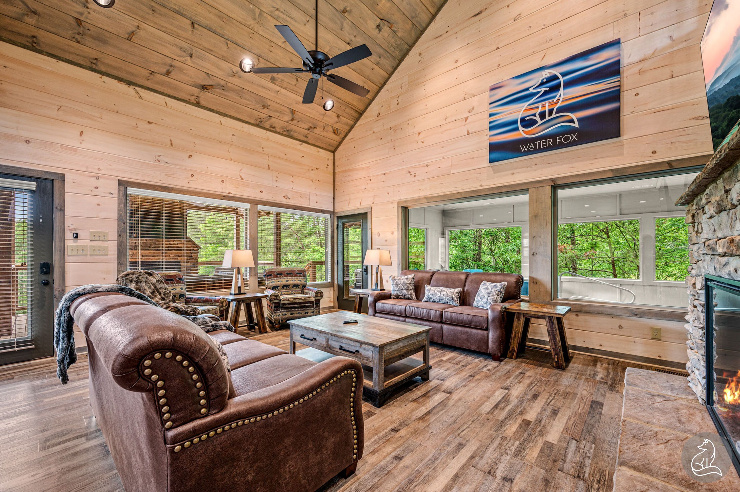A spacious living room with a fireplace, leather furniture, and large windows offering a view of the outdoors.