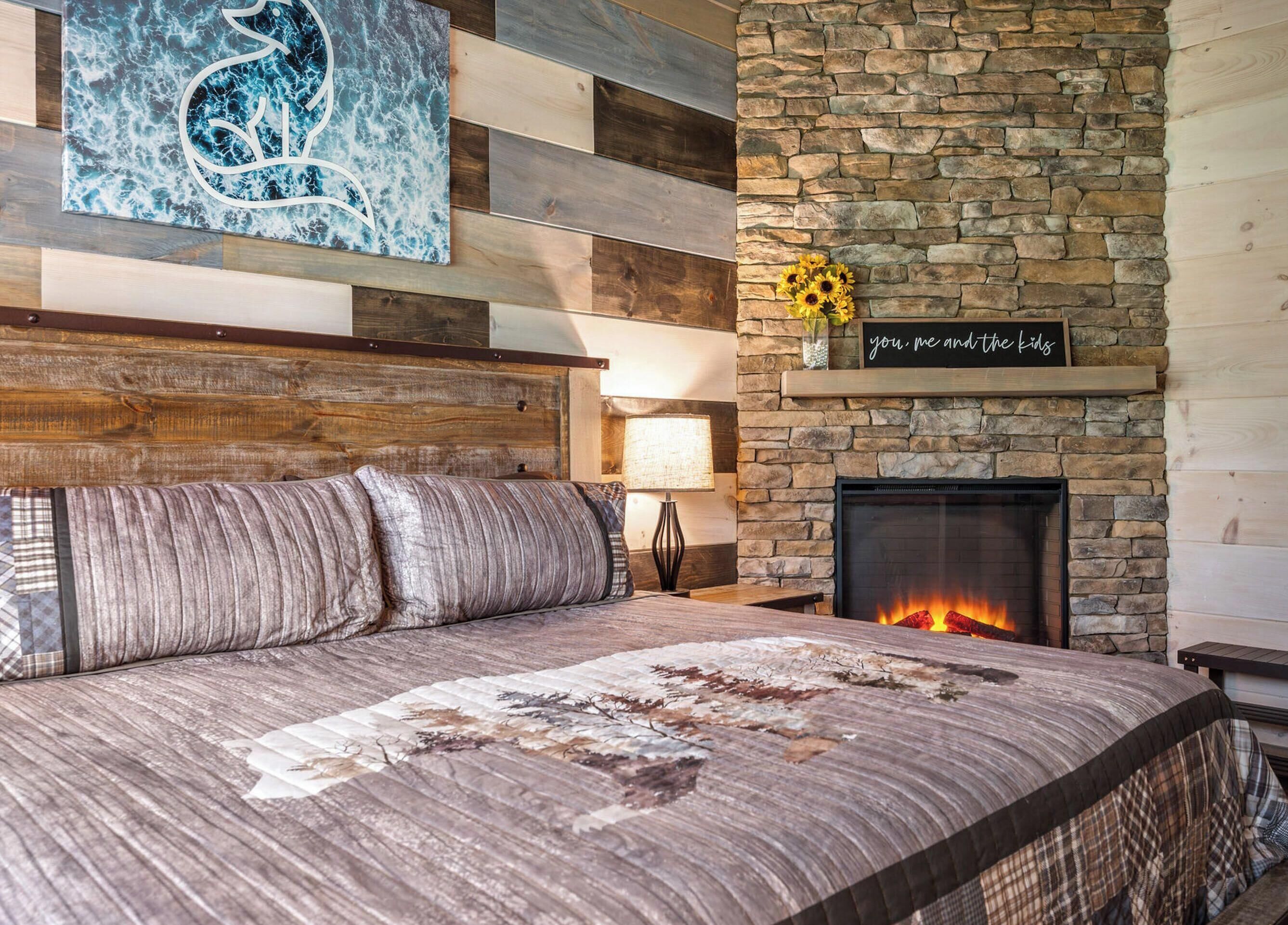 Una camera da letto con camino in pietra, un letto con biancheria a motivi e una parete decorata con un dipinto astratto blu.