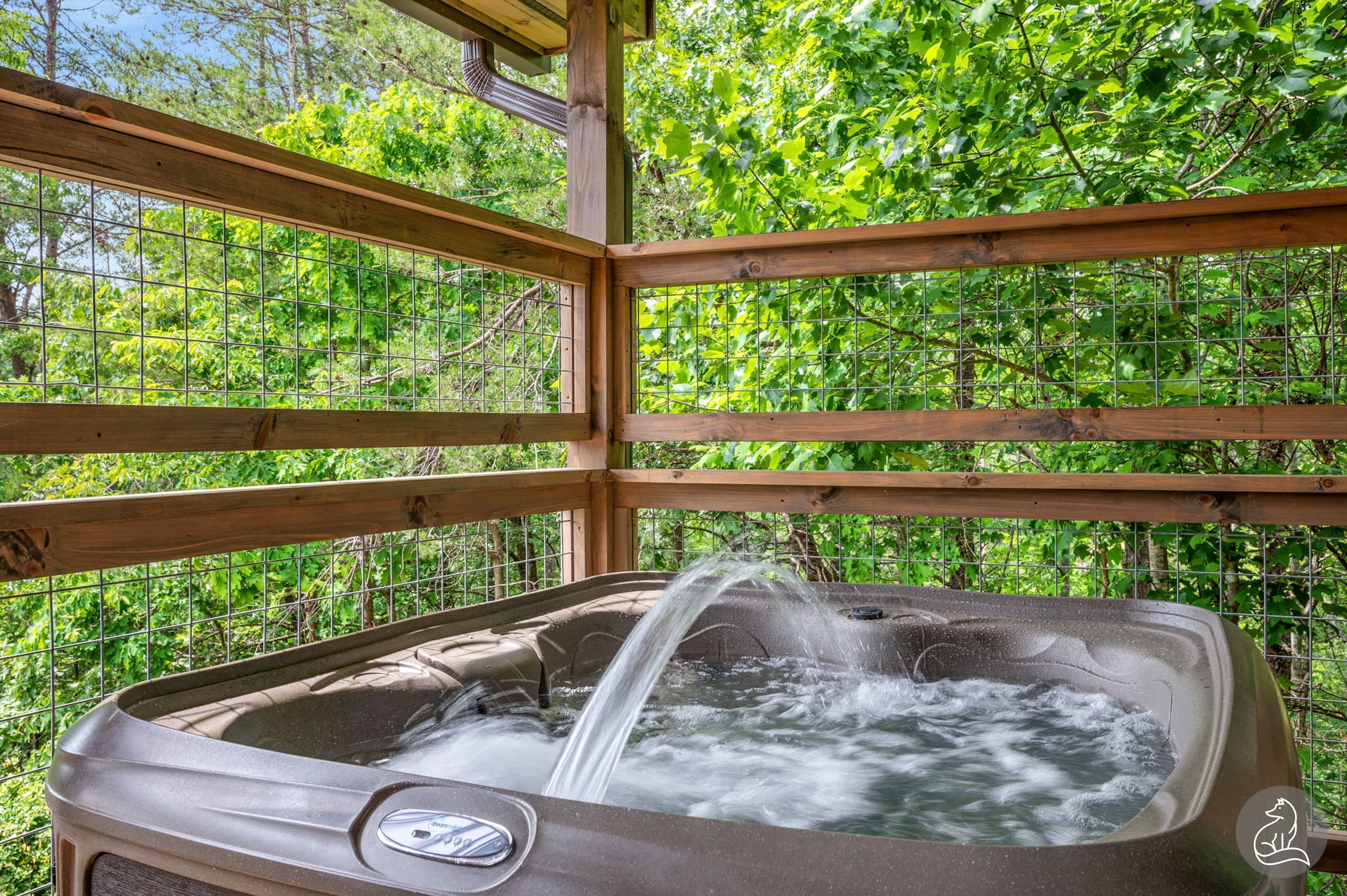 Un jacuzzi con estructura de madera y valla metálica, rodeado de abundante vegetación.