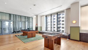 Una habitació àmplia amb una taula de futbolí, una taula de bitlles i un gran finestral que ofereix vista d'un edifici.
