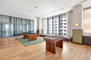 A spacious room with a foosball table, a pool table, and a large window offering a view of a building. - The Crosby Luxury 1BR/1BA in Downtown Miami | 710 (Miami)