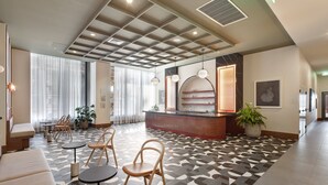Rebedor d'hotel amb taulell de recepció, zona de seients i grans finestres.