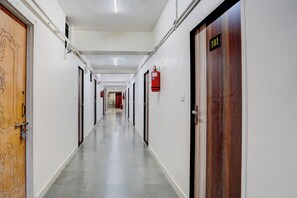 A corridor with doors on both sides, a fire extinguisher mounted on the wall, and a door labeled '101'. - Collection O Prahlad Nagar Road (Ahmedabad)