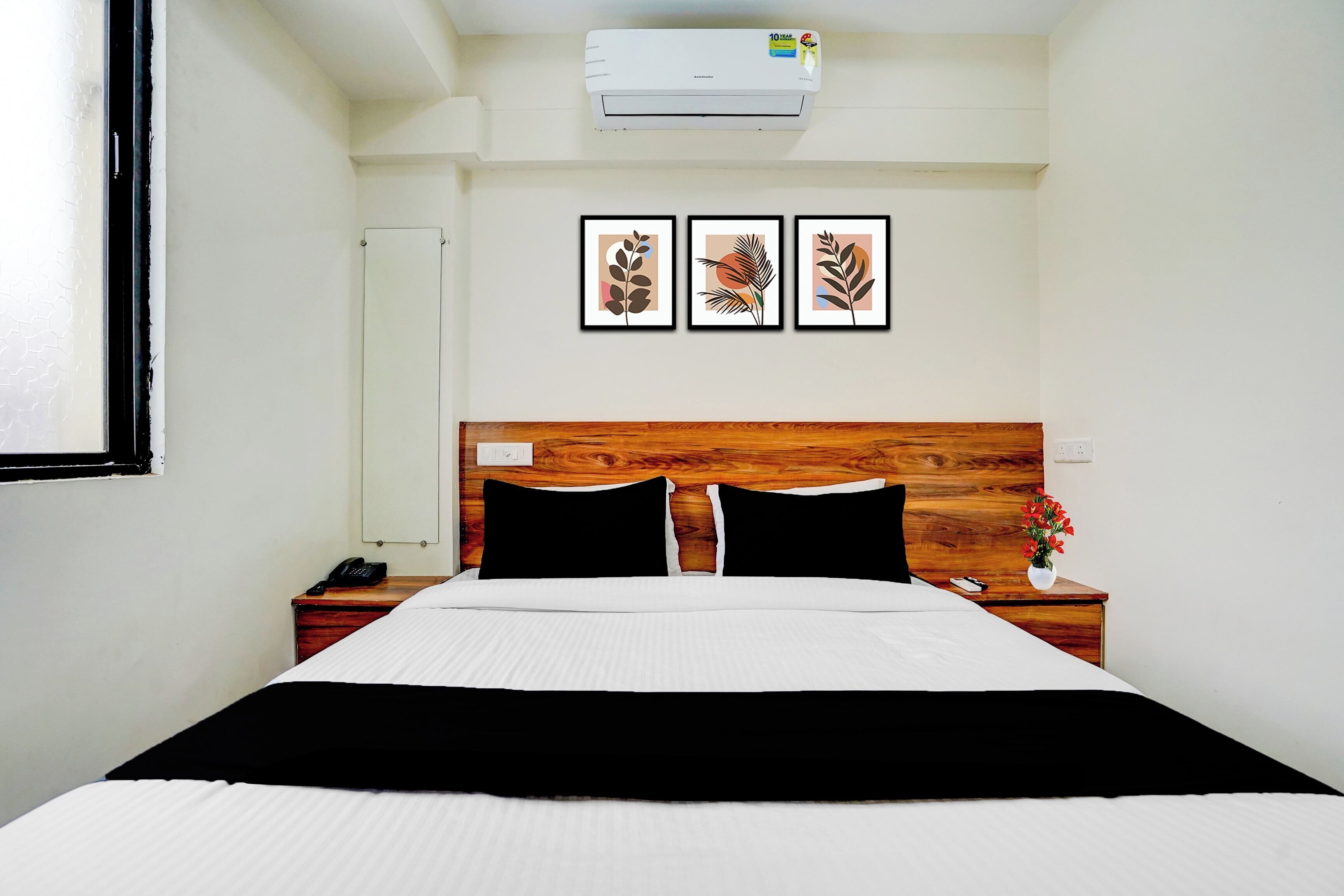 A hotel room with a bed, a nightstand, a phone, a vase with flowers, and three framed pictures on the wall.