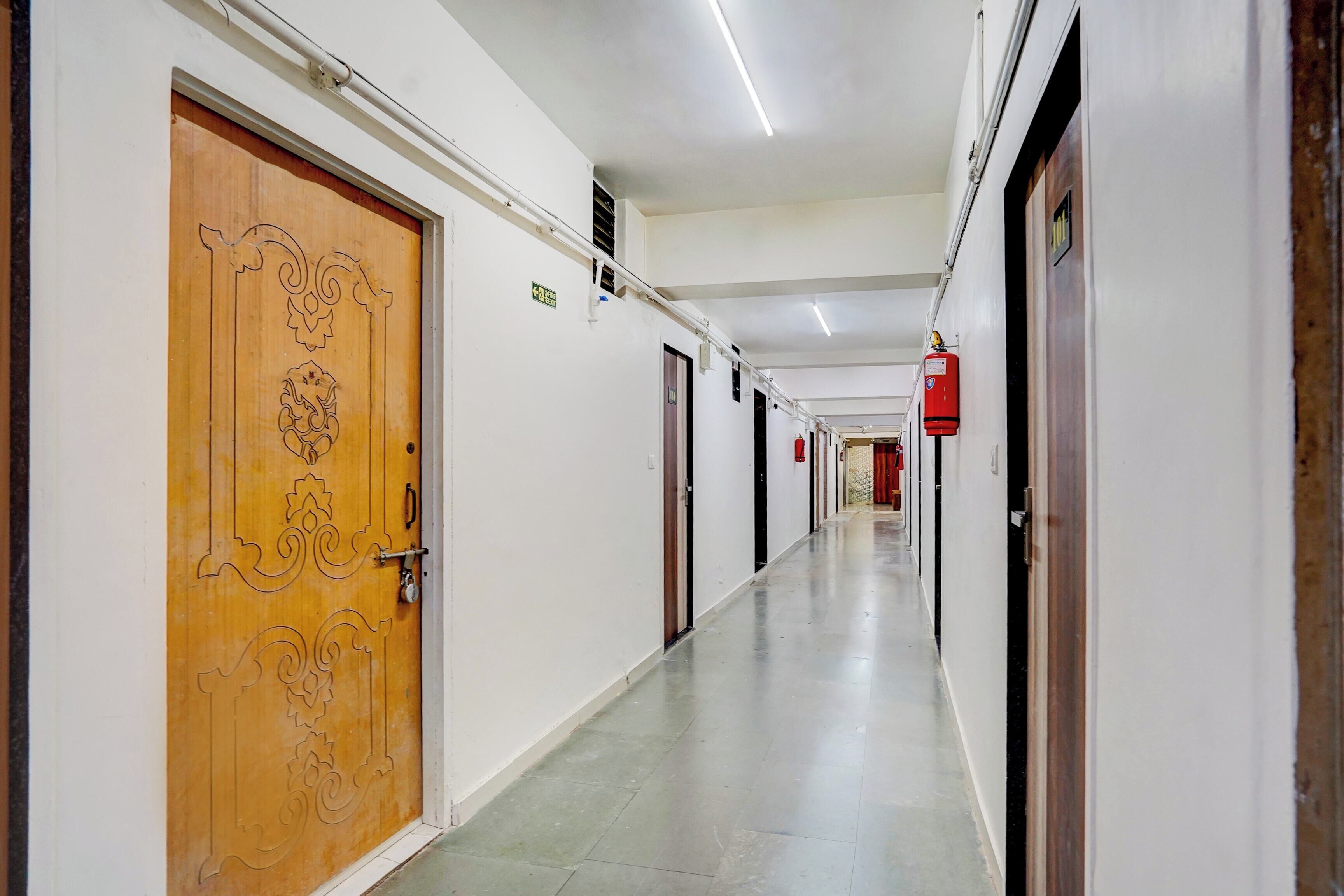 A long, narrow hallway with doors on both sides, a fire extinguisher mounted on the wall, and a ceiling light fixture.