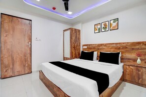 Een slaapkamer met een houten hoofdeinde, een bed met witte beddengoed en zwarte accenten, een houten kledingkast en een wand met drie ingelijste kunstwerken.