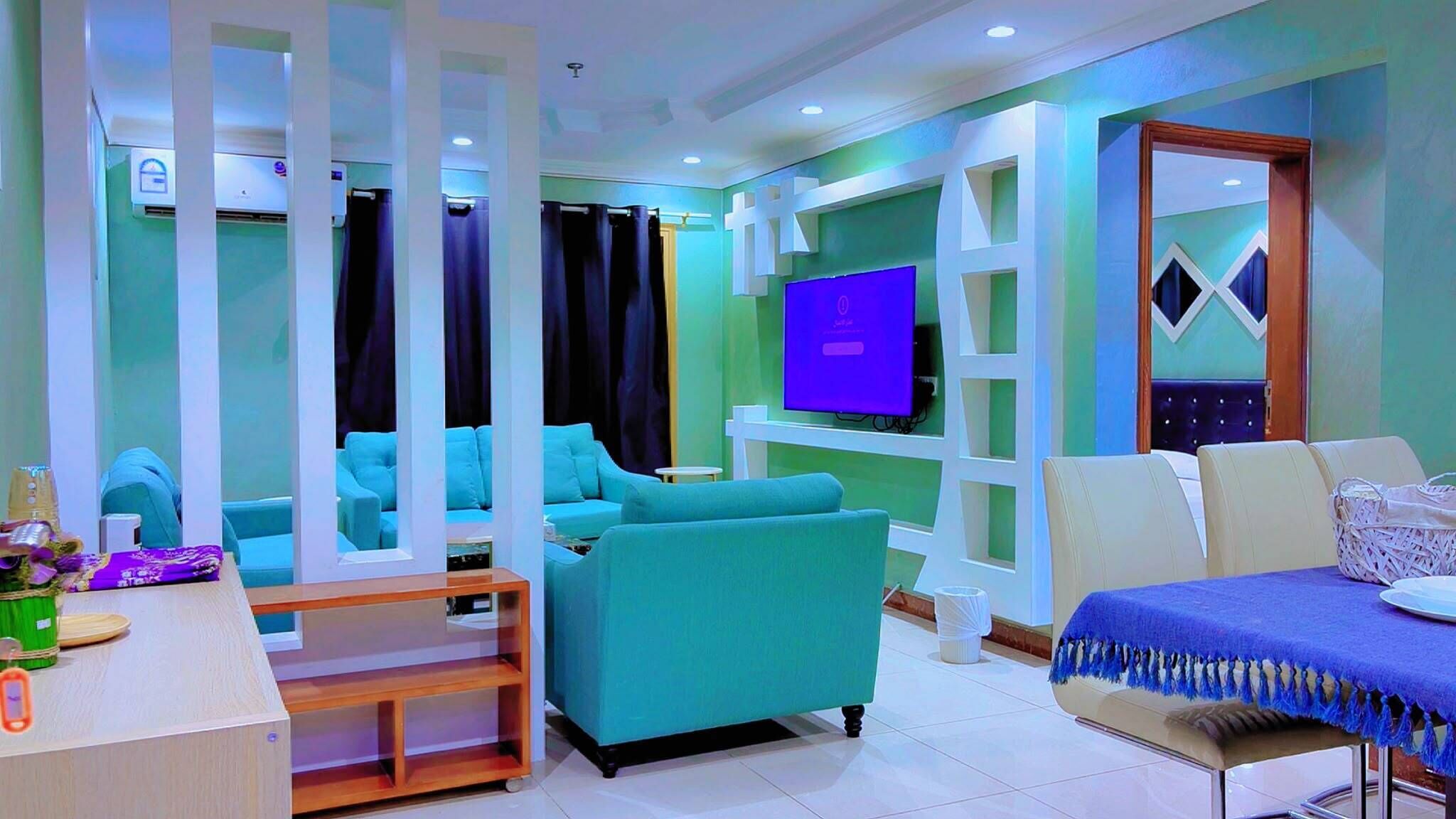 A modern living room with teal sofas, a flat-screen TV, and a wooden coffee table.