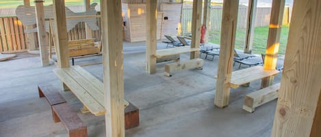 A covered outdoor area with wooden benches and picnic tables, a wooden deck, and a view of the beach.